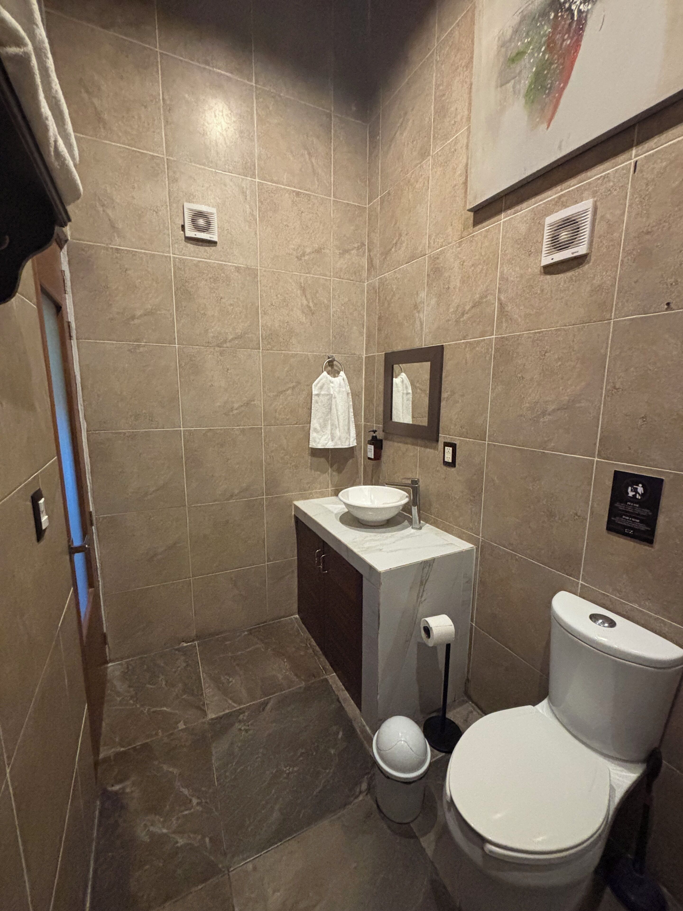 Een compacte badkamer met een wit wastafel, meubel, toilet en een handdoek aan de muur.