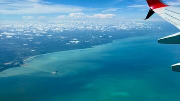 Asa de avião com vista para um mar azul-turquesa e um céu cheio de nuvens.