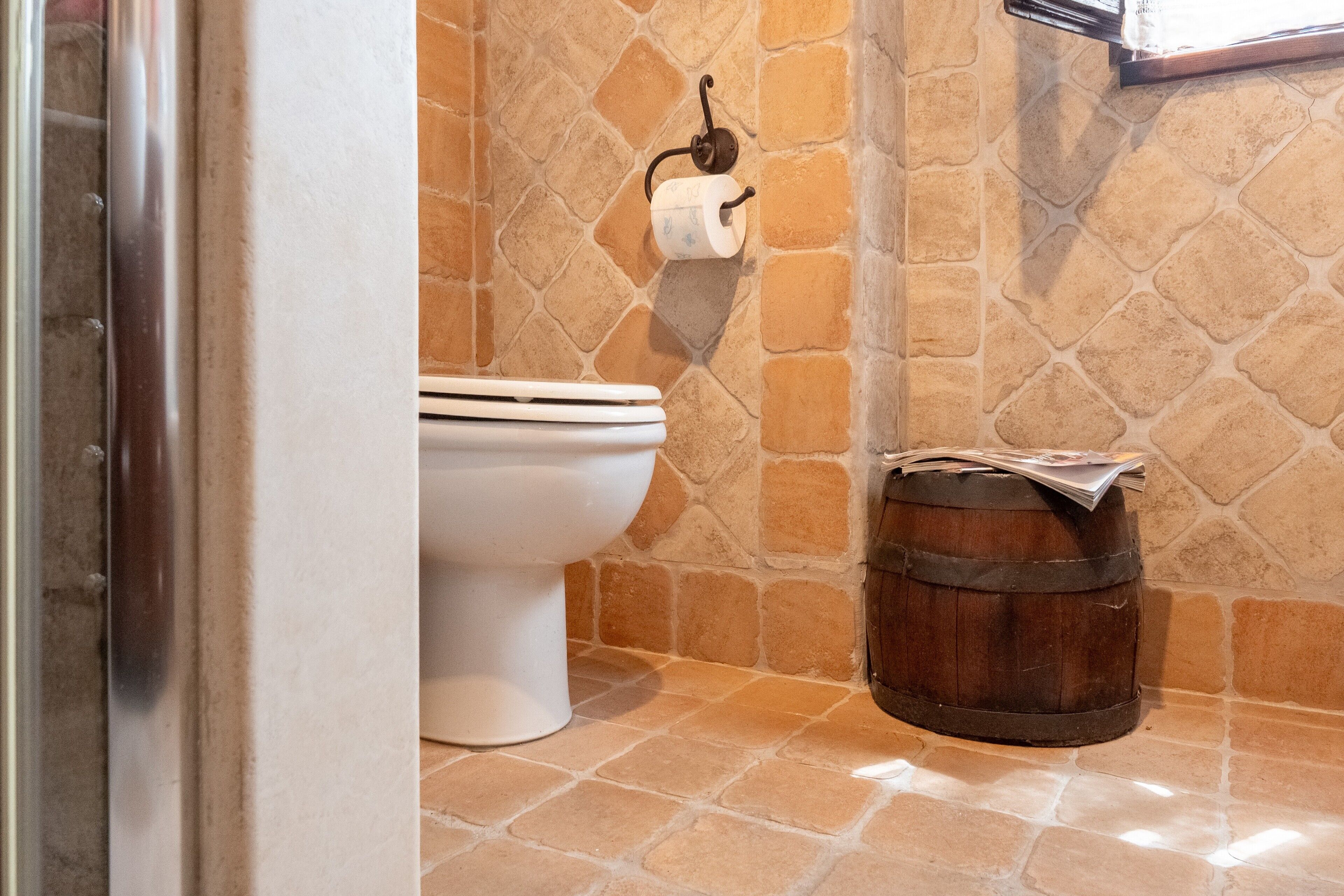 Ein Badezimmer mit Toilette, Papierhalter und einem Holzfass.