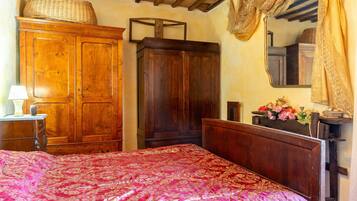 A bedroom with a large wooden bed, a wardrobe, a mirror, and a small table with a lamp.