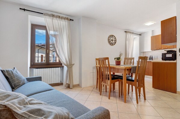 A living room with a sofa, dining table, chairs, a clock, and a kitchen area with cabinets and appliances.