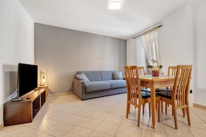 Un salon comprenant un canapé, un téléviseur, une table à manger en bois, des chaises et une petite table d’appoint.
