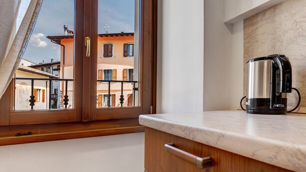 Eine Küche mit Kaffeemaschine, Holzschränken und Blick auf Gebäude durch ein Fenster.