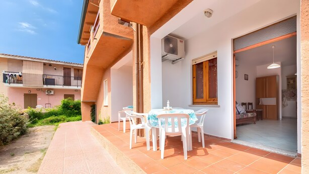 A patio with a table and chairs, an air conditioning unit, and a view of a building with balconies.