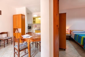 Une pièce comprenant une table à manger, des chaises, un lit, une armoire en bois et un coin cuisine.