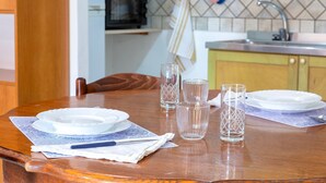 A dining table set with plates, glasses, and a napkin, with a kitchen in the background.