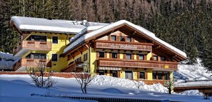 En mangesidet lodge med balkoner, snærede omgivelser og en skov i baggrunden.