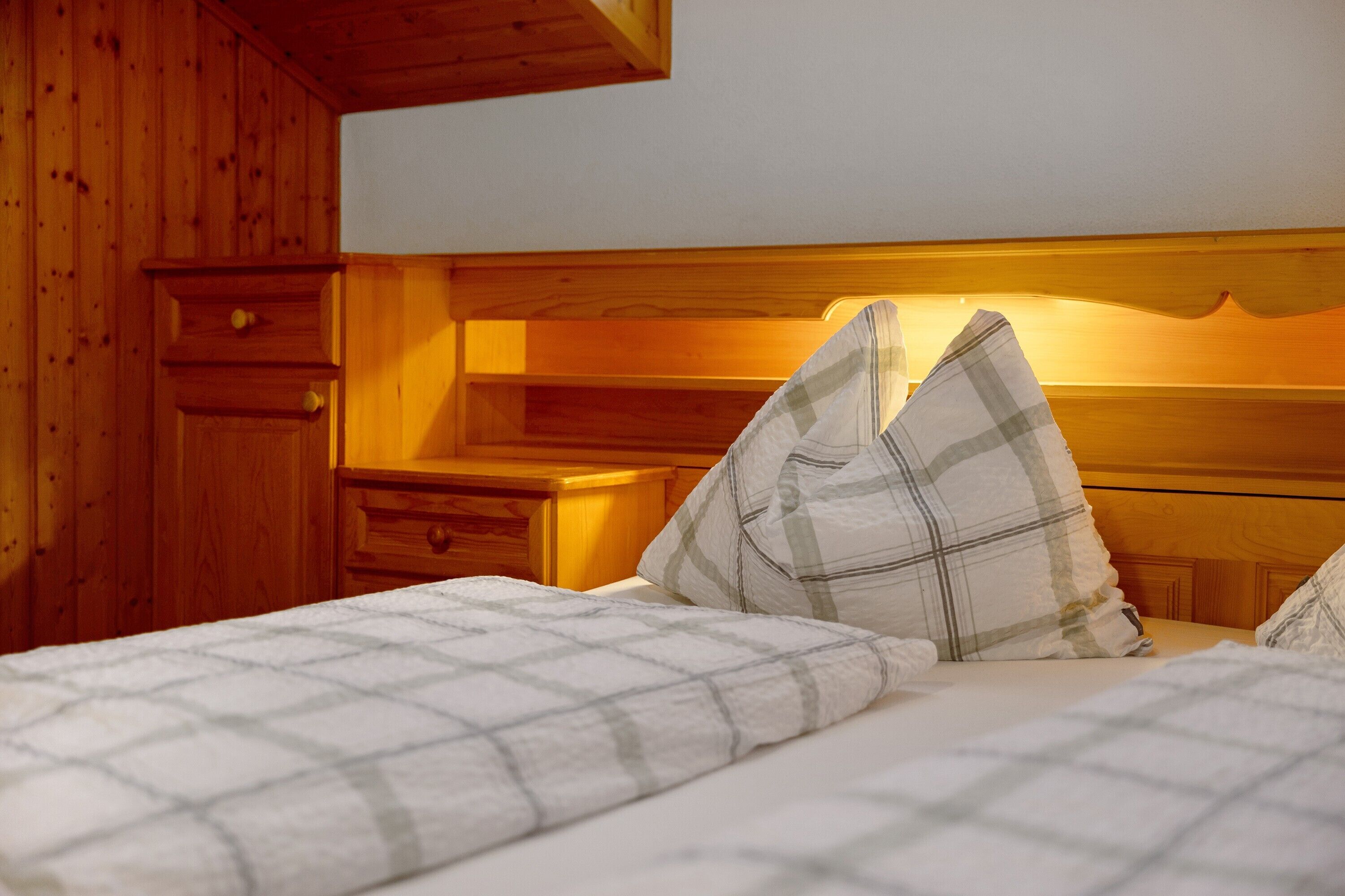 Een slaapkamer in chaletstijl met een bed, twee kussens, een nachtkastje en een houten ladekast.