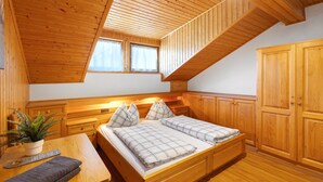 A wooden room with a bed, bedside tables, a plant, and a window.