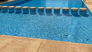 Una piscina con agua azul cristalina, rodeada por una terraza con baldosas.