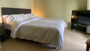 Una habitación de hotel con cama, mesita de noche, lámpara, televisor y televisor de pantalla plana sobre un soporte.