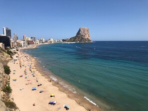 A coastal cityscape with a beach, a prominent rocky hill, and a city skyline.
