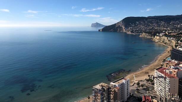 Un paisaje costero con vista despejada al mar, una montaña en la distancia y una zona urbana densamente poblada con rascacielos.