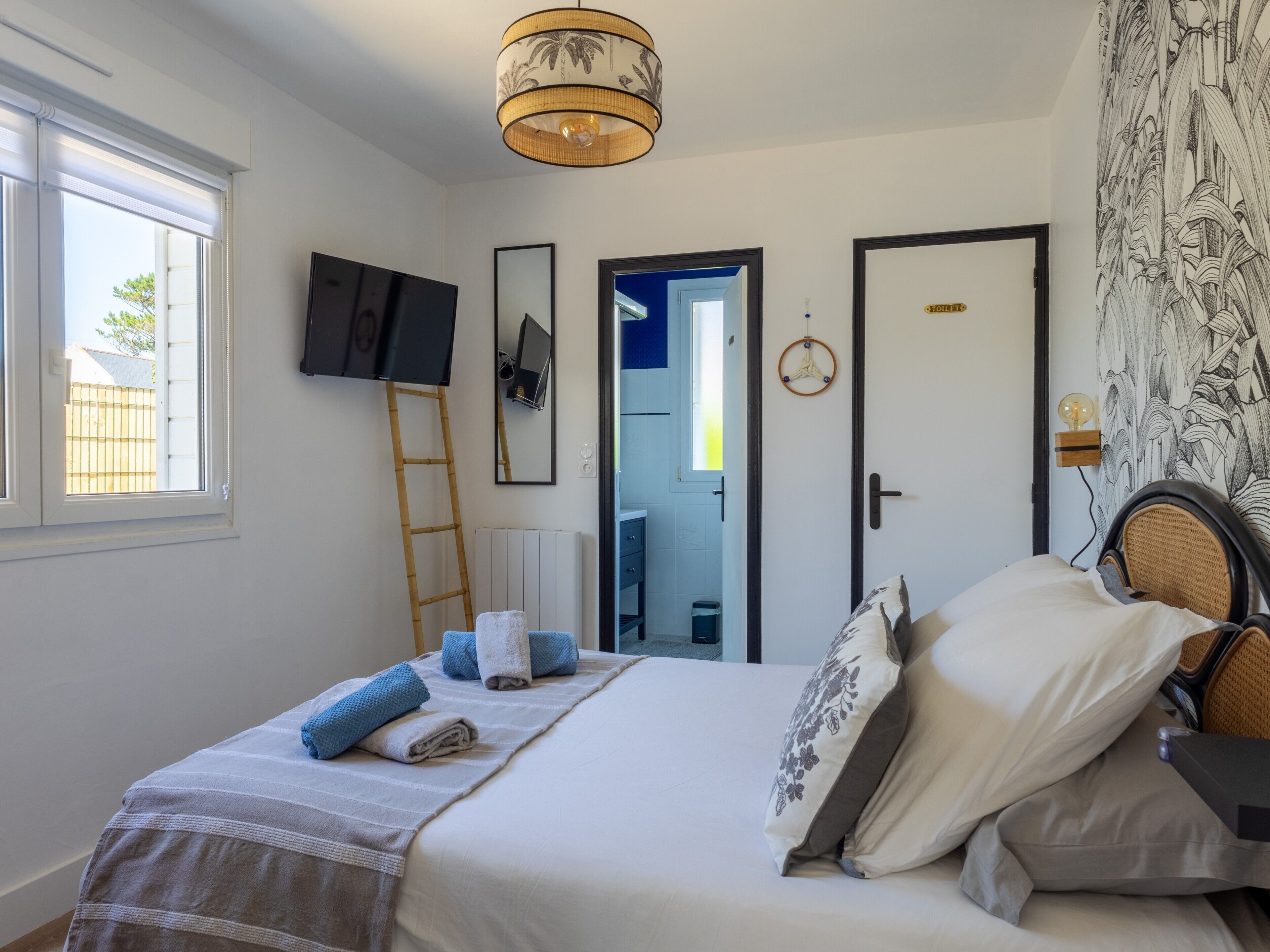 Un dormitorio con una cama, televisión, escalera, puerta y pared con estampado floral.