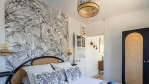Een slaapkamer met een groot bed, een hoofdbord met bladmotief, een nachtkastje met een lamp en een deur met een geweven paneel.