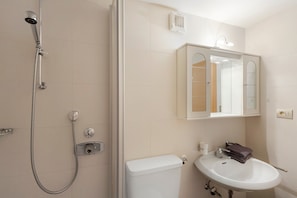 A bathroom with a shower, toilet, sink, and a mirror above the sink.
