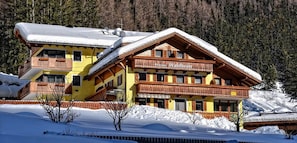 A multi-story lodge with balconies, snow-covered surroundings, and a forested backdrop.