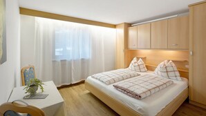 Een slaapkamer met een bed, een bureau, een stoel, een raam met gordijnen en houten kasten.