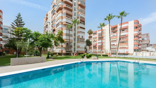 Une piscine entourée d’immeubles d’habitation, de palmiers et d’une pelouse.