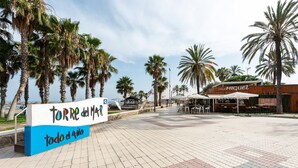 Une promenade dallée bordée de palmiers, un panneau indiquant « TORRE del MAR, ouvert toute l’année », et un bâtiment portant l’inscription « CASA MICUEL ».