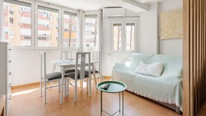 Une pièce comprenant une table à manger, des chaises, un canapé, une petite table d’appoint et une fenêtre donnant sur des immeubles.