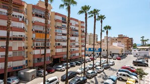Un parking à plusieurs étages où sont garées plusieurs voitures, entouré de palmiers et d’immeubles dotés de balcons.