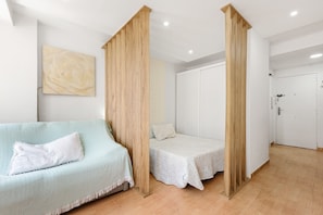 A room with a light blue sofa, two single beds, wooden pillars, a white door, and a large abstract painting on the wall. - Studio 'Sonia' with Shared Pool, Wi-Fi and Air Conditioning (Torre del Mar)