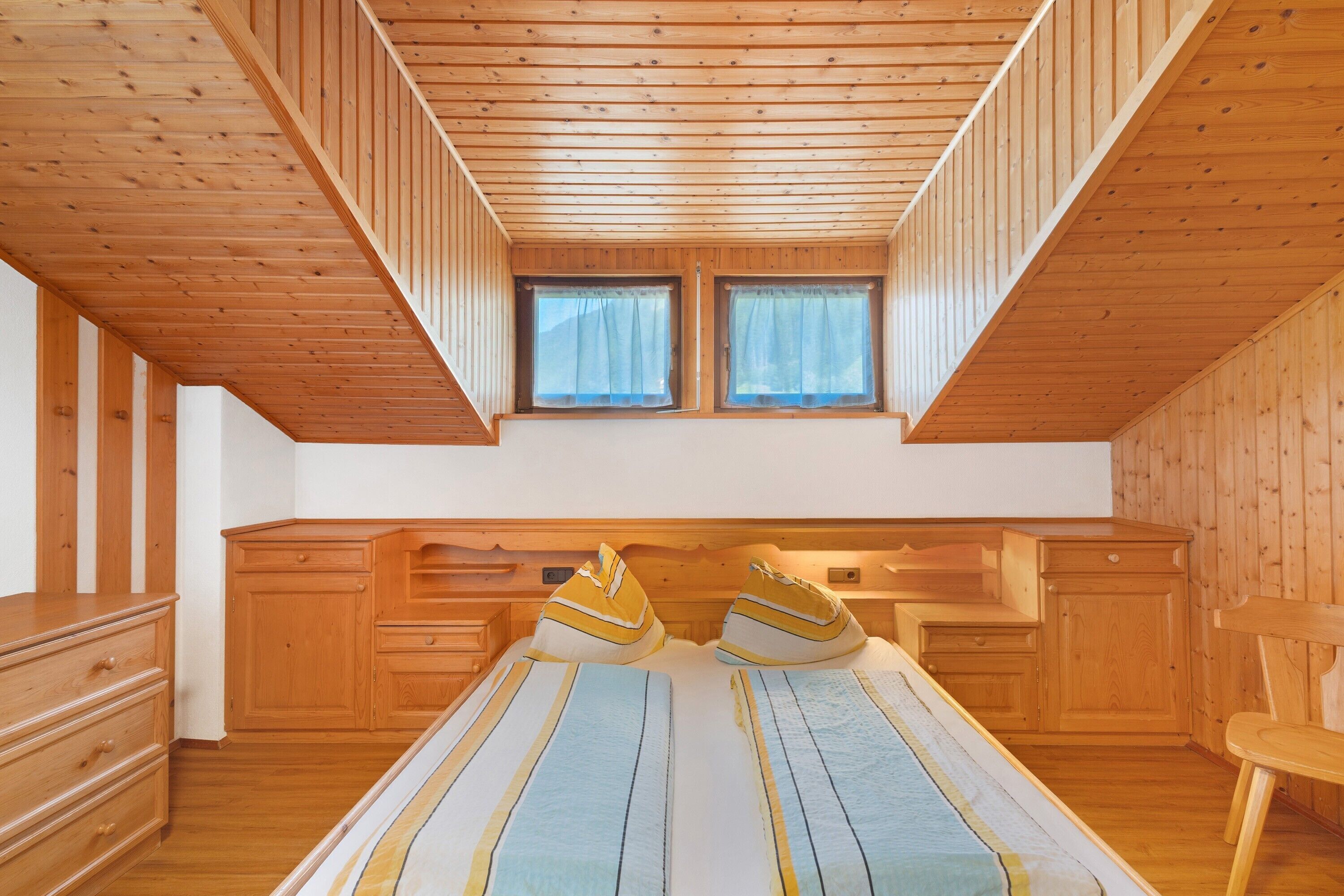A wooden-paneled room with a bed, a desk, and a window.