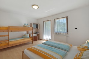 A room with bunk beds, a desk, a television, and a window with curtains.