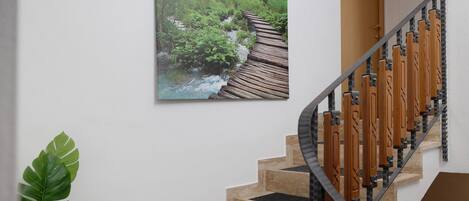 A staircase with wooden handrails and beige steps, a wall-mounted picture of a forest stream, and a potted plant.