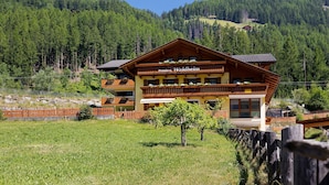 A multi-story building with a sign reading 'Pension Waldheim,' surrounded by a wooden fence, a small tree, and a mountainous backdrop. - Room 'Pension Waldheim  3' with Mountain View, Shared Garden and Wi-Fi (Ahrntal)