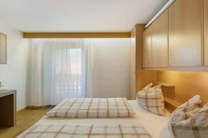 A bedroom with a bed, pillows, a desk, and a window with curtains.