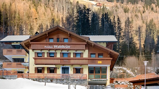 A multi-story building with balconies, labeled 'Pension Waldheim,' surrounded by a snowy landscape and forested hills. - Room 'Pension Waldheim  3' with Mountain View, Shared Garden and Wi-Fi (Ahrntal)