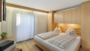 A bedroom with a bed, wooden wardrobe, and a window with curtains. - Room 'Pension Waldheim  3' with Mountain View, Shared Garden and Wi-Fi (Ahrntal)