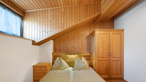 Ein Schlafzimmer mit Holzbalkendecke, einem Bett mit Kissen, einem Nachttisch und einem Kleiderschrank.