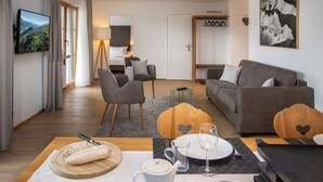 A modern living room with a sofa, chairs, a dining table set for two, and a TV mounted on the wall. - La Siala Apt.17 by Interhome (Falera)