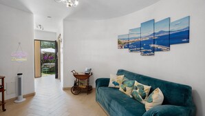 Un salon avec un canapé de couleur turquoise, une œuvre d’art accrochée au mur et un ventilateur sur pied.