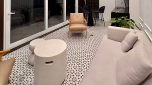 A modern living room with a sofa, a chair, and a small table. There is a sliding glass door leading to an outdoor area.