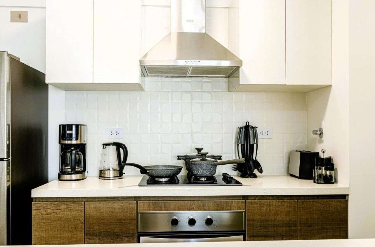 Une cuisine moderne avec des meubles blancs, une hotte de cuisinière en acier inoxydable, une machine à café, une bouilloire, une poêle et un grille-pain.