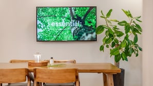 A dining area with a wooden table and chairs, a flat-screen TV mounted on the wall displaying a nature scene, and a potted plant to the right. - Chuncheon Haven Forest Pension (Chuncheon)