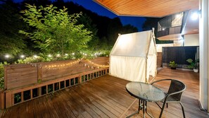 Un terrazzo in legno con tavolo e sedie, una tenda e luci decorative.