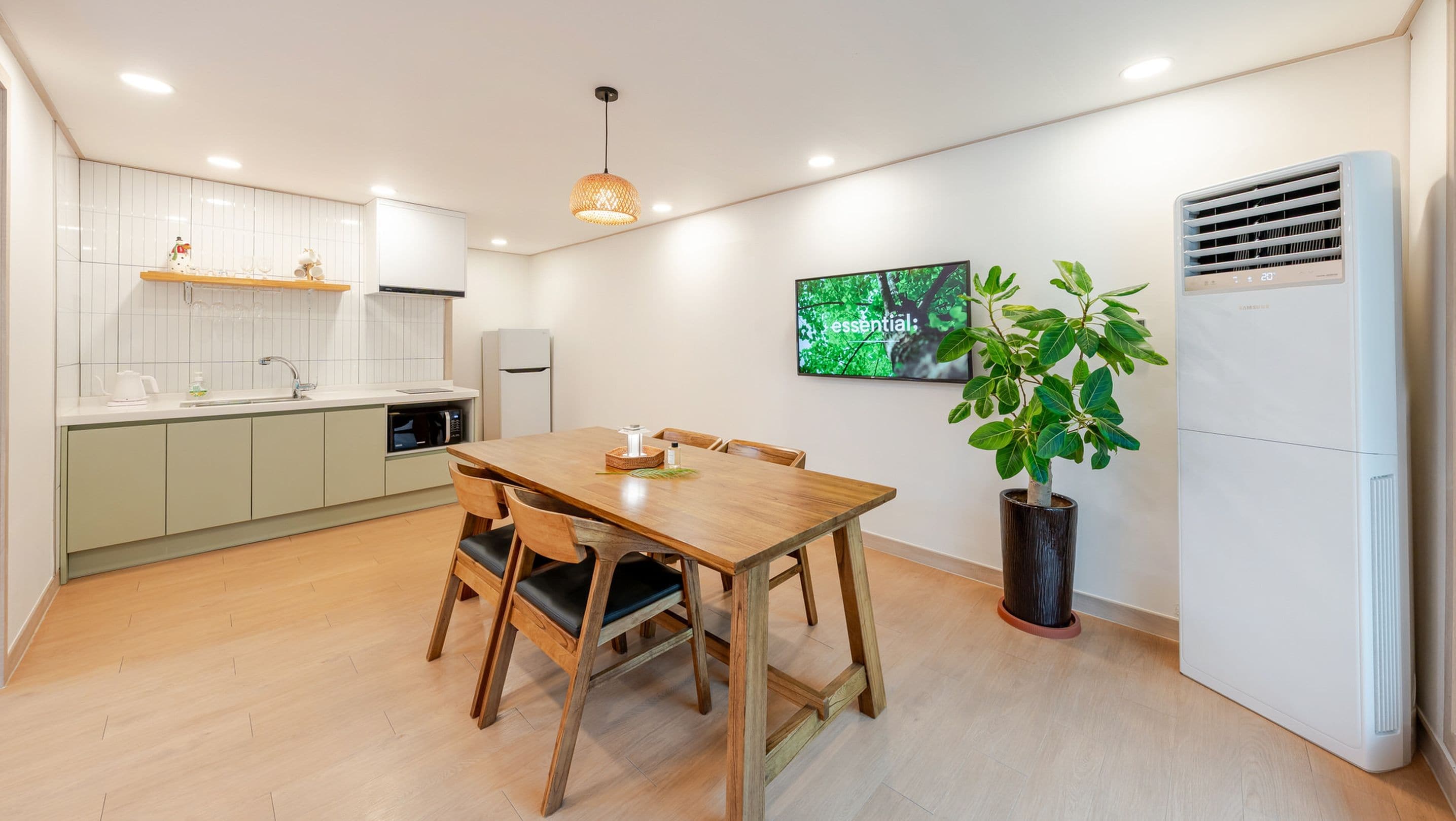 Een moderne keuken met een eethoek, met een houten tafel en stoelen, een ingebouwde oven en een grote flatscreen televisie aan de muur.