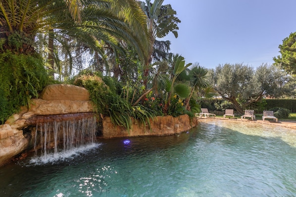 A pool with a waterfall feature, surrounded by lush greenery and palm trees.