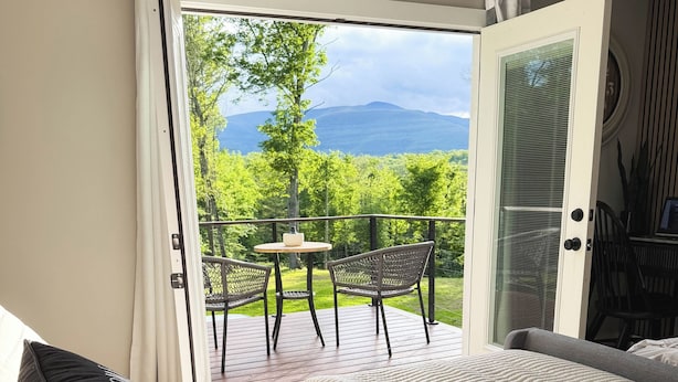 Ein Schlafzimmer mit Bett, Blick auf einen Balkon mit Tisch und Stühlen sowie einer Tür, die nach draußen führt.