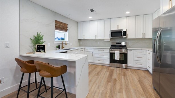 A modern kitchen with white cabinets, stainless steel appliances, a central island with bar stools, and a window with blinds.