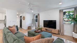 A modern living room with a large green sofa, a flat-screen TV, and a ceiling fan.