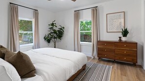A bedroom with a bed, a dresser, a ceiling fan, and a window with curtains.