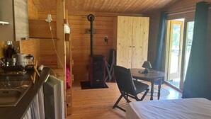 Ein Blockhaus-Interieur mit Küchenzeile, einem Esstisch mit Stuhl, einem Bett und einem großen Fenster.