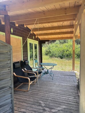 A covered outdoor seating area with wooden flooring, a table, and chairs.