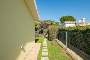 A pathway leading to a house with a white exterior, a green fence, and a clear blue sky.